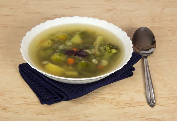 Plaat van plantaardige soep, lepel en blauwe servet op een tafel — Stockfoto