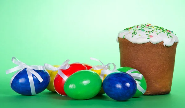 The Easter eggs decorated with a ribbon and a cake on a green background — Stock Photo, Image