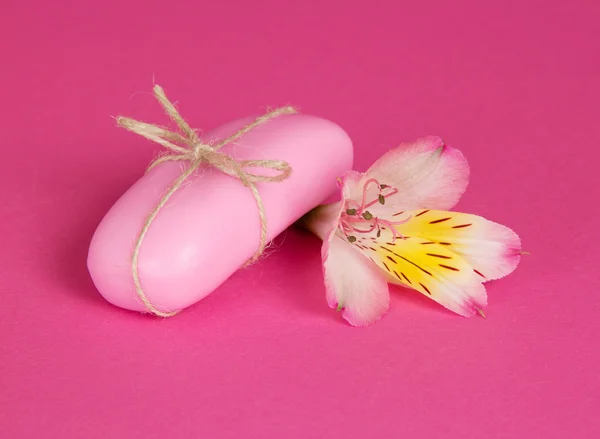 Kawałek mydła toaletowego związany przez sznurka i kwiaty Alstremeria, na tle różowy — Zdjęcie stockowe