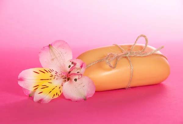 Stück der Toilettenseife, die durch einen Faden verbunden ist, und Blume auf rosa Hintergrund — Stockfoto