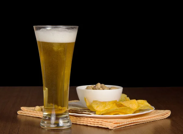 Schotel met chips, pimpernoten (pistaches) en zoute vis, een glas met bier en een servet op een tafel — Stockfoto