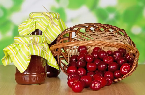 Jars of jam, sweet cherries which dropped out of a basket — Stock Photo, Image