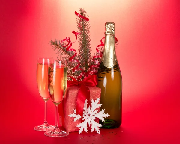 Champagne, fir-tree branch with tinsel, gift box, snowflake on a red background — Stock Photo, Image