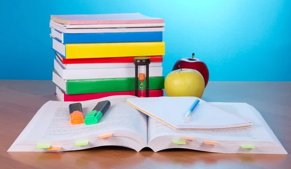 Le livre ouvert avec les signets, le cahier d'exercices la plume et les marqueurs, la pile des livres fermés le sablier et les pommes sur la table — Photo