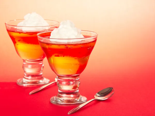 Dos vasos con gelatina y crema batida, cucharas en el rosa —  Fotos de Stock