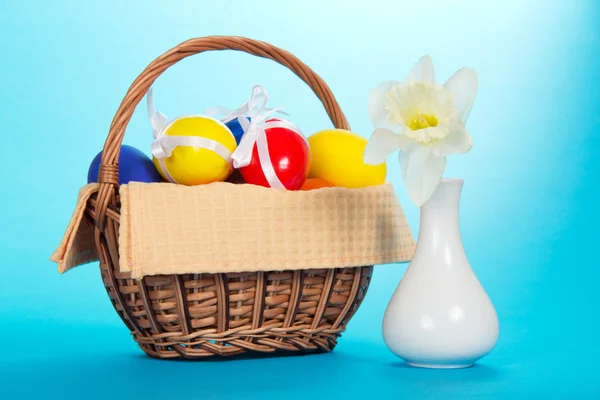 Huevos de Pascua en una cesta con una servilleta y un jarrón con narciso, en el azul —  Fotos de Stock