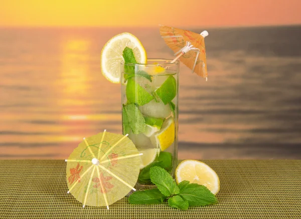 Mojito with umbrellas, a lemon on a green bamboo cloth against the sunset — Stock Photo, Image