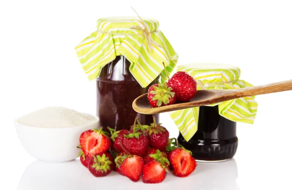 Jars of jam, cup with sugar, a heap the strawberries and strawberries in a spoon — Stock Photo, Image