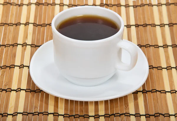 Чашка кофе с блюдцем против бамбуковой салфетки — стоковое фото