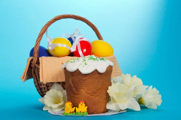 Eggs in a basket, an Easter cake, marzipan chickens and a bouquet of white narcissuses, on the blue — Stock Photo, Image