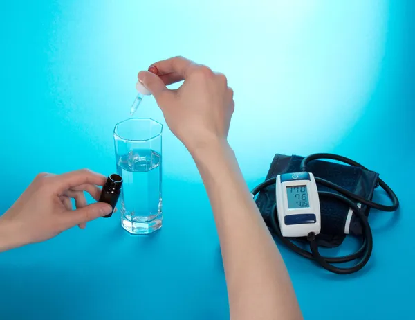 Hand mit medizinischen Tropfen, ein Glas mit Wasser und ein Tonometer auf blauem Hintergrund — Stockfoto
