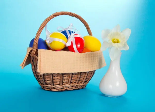 White narcissus in a ceramic vase and eggs in a wattled basket, on the blue — Stock Photo, Image