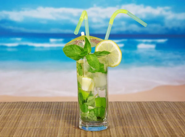 Bevanda fredda con fetta di limone, menta, su un panno di bambù contro il mare — Foto Stock