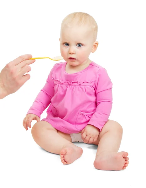 Lief klein babymeisje in een roze jurk eet van een lepel geïsoleerd op wit — Stockfoto
