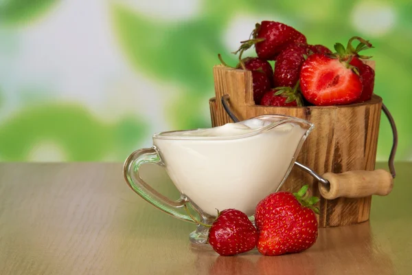 Strawberry in a bucket, and a cup with cream on a table Stock Photo
