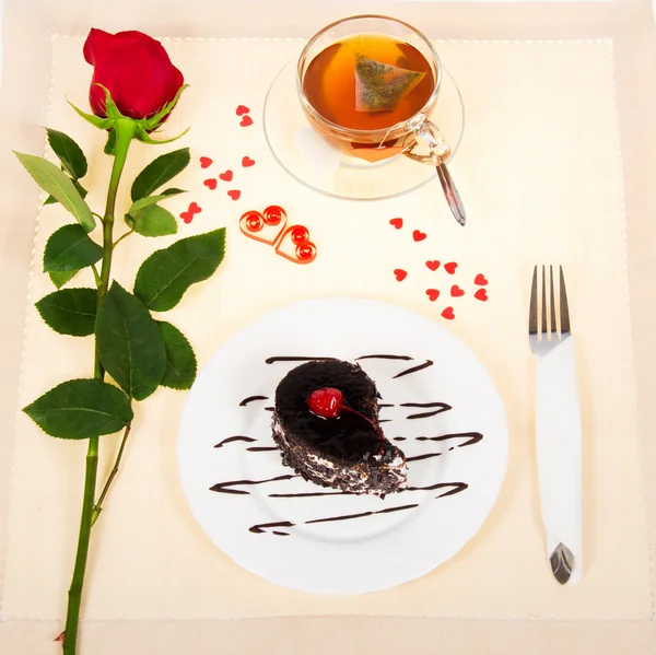 Chocolate cake, hot tea and red rose on a cloth decorated with hearts in Valentine's day Stock Image