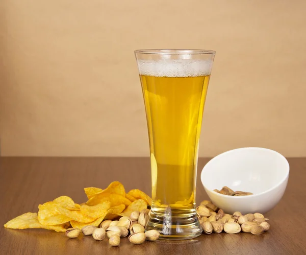 Glass with beer, golden chips and the pistachios which have dropped out of a bowl, against paper Stock Image