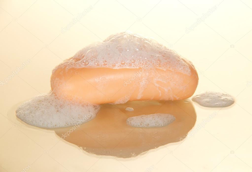 Piece of soap, orange color, with bubbles, on a beige background