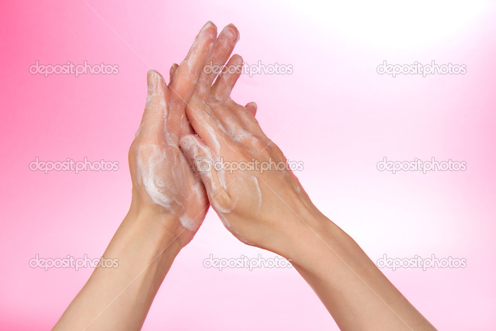 Hands in the foam of soap on a pink background