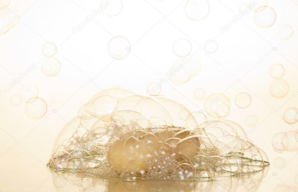 Transparent soap bubbles and piece of soap on a beige background