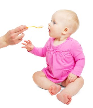 Tatlı küçük bebek kız pembe elbise giymiş bir kaşık beyaz izole yiyor.