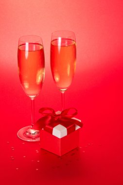 Şampanya ve bir küçük hediye kutu kırmızı bir arka plan üzerinde iki ayaklı büyük kadehler