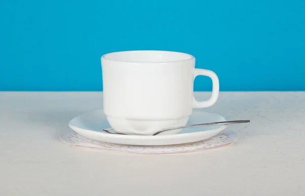 Cup, saucer and spoon on a white cloth, on a blue background — Stock Photo, Image