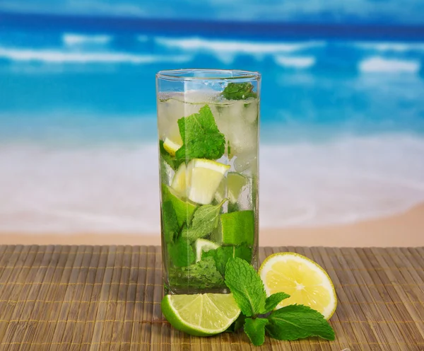 Glass med mojito, saftig lime og et peppermynteblad på en bambusduk mot havet – stockfoto