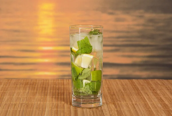 Green alcoholic cocktail from a citrus and mint, on a bamboo cloth against the sunset — Stock Photo, Image