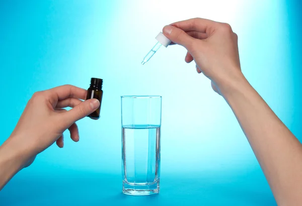 De hand, druipend medische druppels in een glas met water op een blauwe achtergrond — Stockfoto