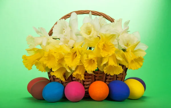 Bouquet of white and yellow narcissuses in a wattled basket and Easter eggs, on a green background — Stock Photo, Image