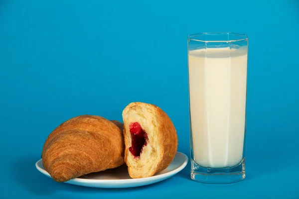 Verse croissants op een schotel en melk op een blauwe achtergrond — Stockfoto