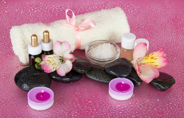 Aceite aromático, sal, velas, piedras, flores, sobre un fondo rosa húmedo —  Fotos de Stock