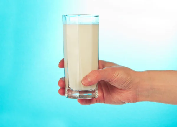Glass of fresh cold milk in a hand on a blue background — Stockfoto