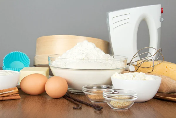Αλεύρι, γαλακτοκομικά προϊόντα, αυγά, μπαχαρικά και μίξερ σε έναν πίνακα, σε γκρι φόντο — Φωτογραφία Αρχείου