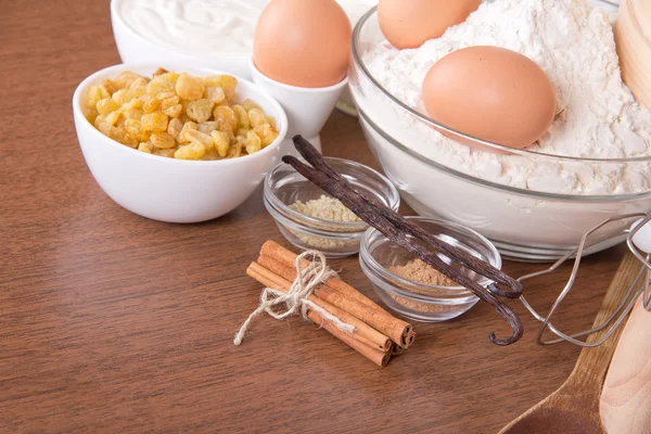 Russin, sesamfrö, pinnar kanel och vanilj baljor, ett mjöl, gräddfil och ägg på ett bord — Stockfoto