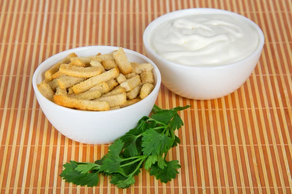 Bowl with sour cream, a bowl with toasts and parsley,on a beige bamboo cloth — Stock Photo, Image