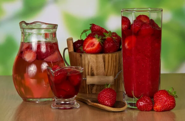 La jarra con la bebida, la fresa en el cubo, en el vaso, la cuchara de madera las bayas cerca sobre la mesa — Foto de Stock