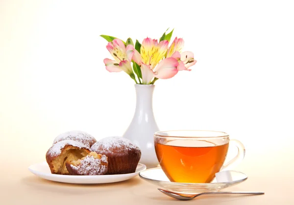 Tasse avec thé, cuillère et cupcakes sur un plat, sur le beige — Photo