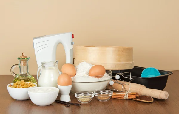 Süt ve süt ürünleri, yumurta, un, ayçiçek yağı, Kuru üzüm ve bej renkli arka plan üzerinde pişirme çanağı — Stok fotoğraf