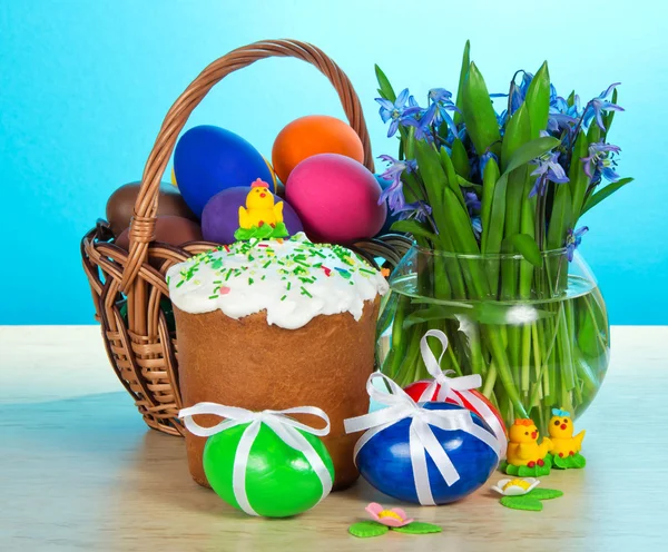 Feestelijke Pasen voedsel en vaas met de bloemen op een tafel, op een blauwe achtergrond — Stockfoto