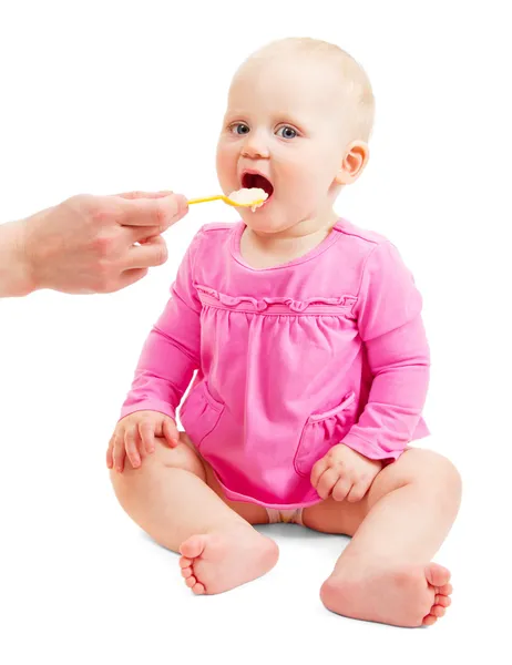 Bella bambina in un vestito rosa mangia da un cucchiaio isolato su bianco — Foto Stock