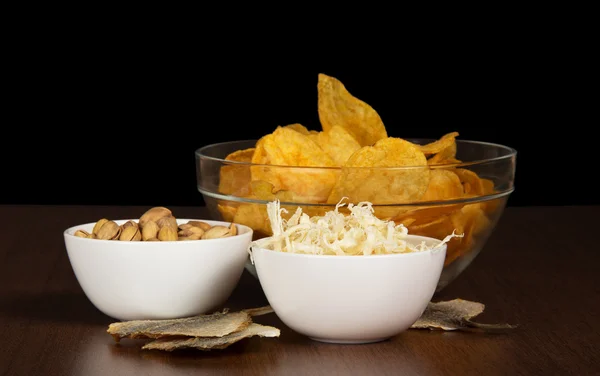 Chips, pistachios, dried squids and salty fish, on the table — Stock Photo, Image