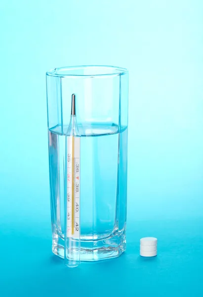 Mercury thermometer, glass with water and tablets on a blue background — Stock Photo, Image