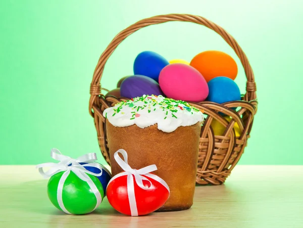 Colourful eggs, basket and Easter on a table, on a green background — Stock Photo, Image