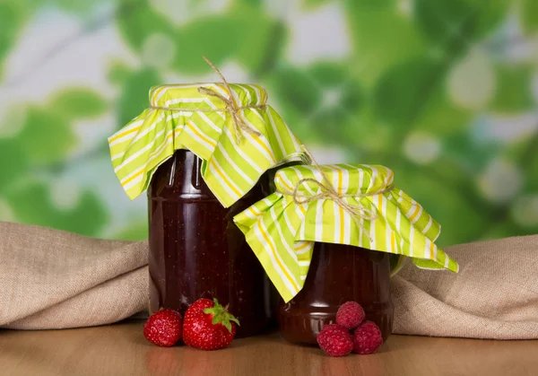 Sklenice džemu, jahody a maliny před plátnem, na stůl — Stock fotografie