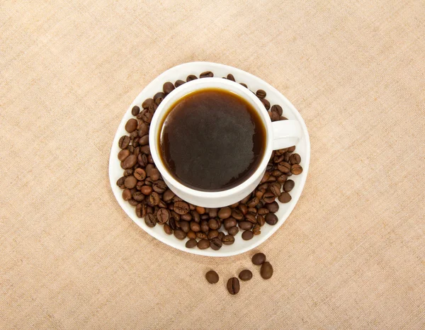 Tasse Kaffee und Untertasse, Kaffeekörner auf beigem Hintergrund — Stockfoto