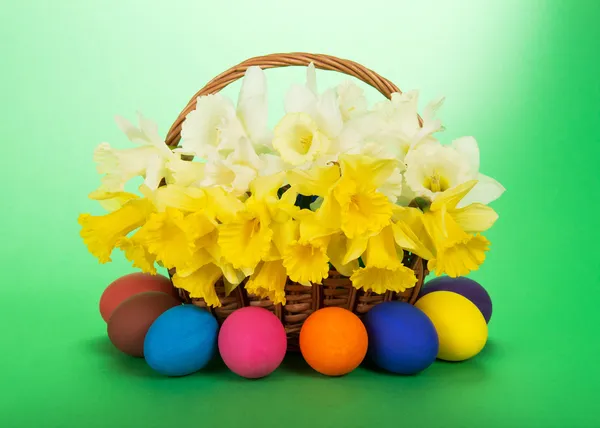 Bouquet of white and yellow narcissuses in a wattled basket and Easter eggs, on a green background — Stock Photo, Image