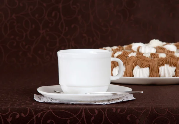 Gateau, cup, saucer and spoon against a brown cloth — Stock Photo, Image