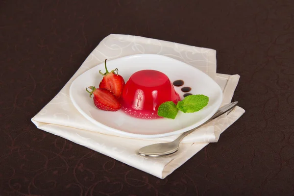 Las gotas del chocolate y la fresa en el plato de la jalea, la cuchara y la servilleta sobre el mantel —  Fotos de Stock